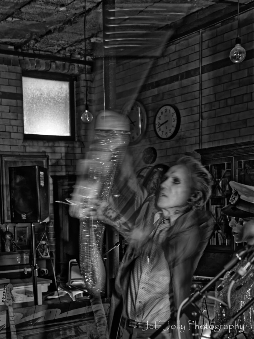 A performer moving a metal tube in a black-and-white long exposure
