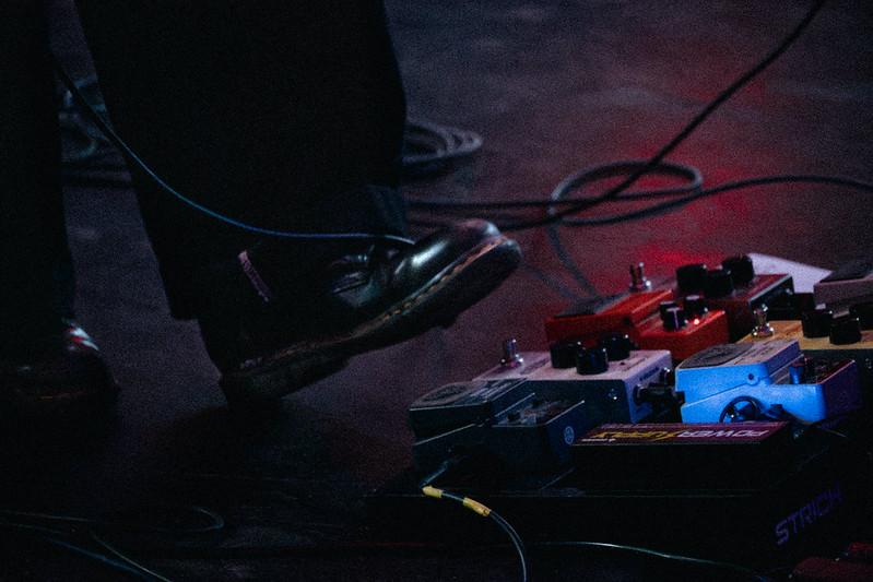 A musician stepping beside a pedalboard during a live set